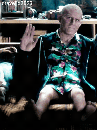 A Man In A Floral Shirt Is Sitting On A Couch And Waving His Hand GIF