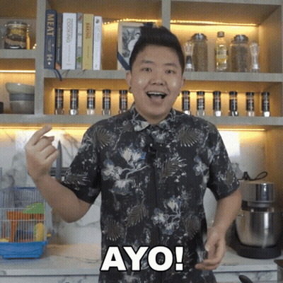 A Man In A Floral Shirt Says Ayo In Front Of A Bookshelf GIF