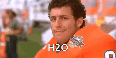 A Man In A Football Uniform Is Sitting On A Field And Smiling At The Camera . GIF