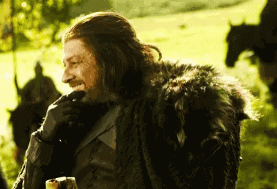 A Man In A Fur Coat Is Smiling In A Field With Horses In The Background GIF