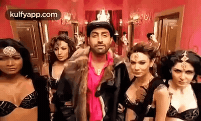 A Man In A Fur Coat Is Standing In Front Of A Group Of Women In Bras . GIF
