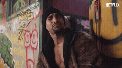 A Man In A Fur Coat Is Standing In Front Of A Wall With Graffiti On It And The Word Netflix On The Bottom GIF