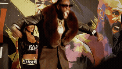 A Man In A Fur Coat Is Standing Next To A Woman Wearing A Manscape Crop Top GIF