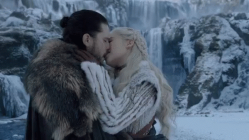 A Man In A Fur Coat Kisses A Woman In Front Of A Waterfall GIF