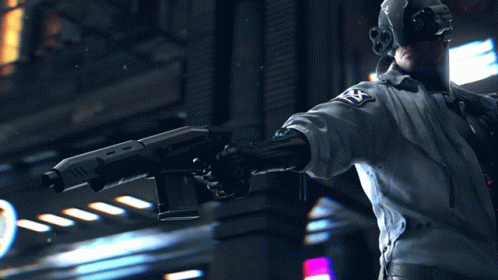 A Man In A Futuristic Outfit Is Holding A Gun With The Letter T On It GIF