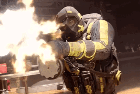 A Man In A Gas Mask Is Holding A Gun With Flames Coming Out Of It 'S Barrel . GIF