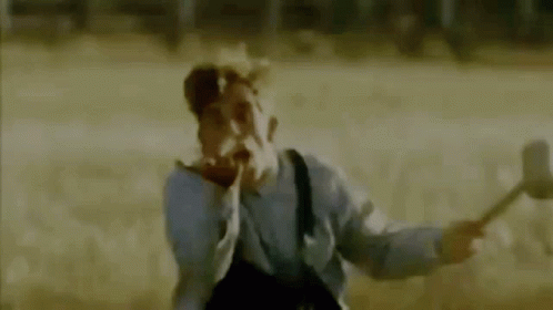A Man In A Gas Mask Is Holding A Hammer In A Field And Making A Funny Face . GIF