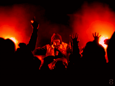 A Man In A Gas Mask Is Singing Into A Microphone In Front Of A Crowd Of People GIF