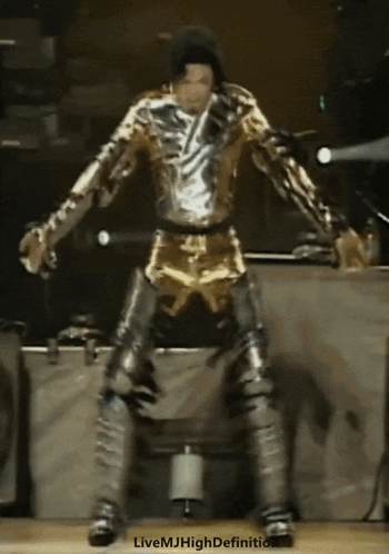 A Man In A Gold And Silver Outfit Is Dancing On Stage GIF