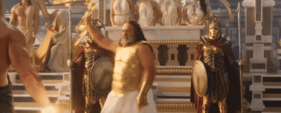 A Man In A Gold Armor Is Standing In Front Of A Statue Of A Greek God . GIF
