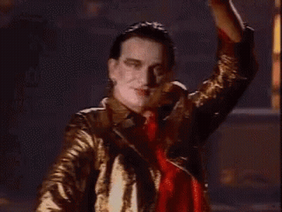 A Man In A Gold Jacket Is Dancing In A Dark Room GIF