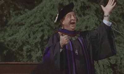 A Man In A Graduation Cap And Gown Is Giving A Speech With His Arms Outstretched . GIF