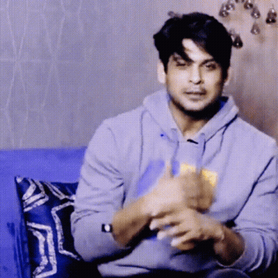 A Man In A Gray Hoodie Is Sitting On A Blue Couch And Eating Chips . GIF