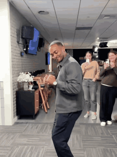 A Man In A Gray Jacket Is Dancing In A Hallway GIF