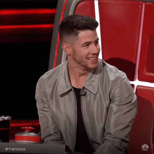 A Man In A Gray Jacket Is Smiling In Front Of A Nbc Sign GIF