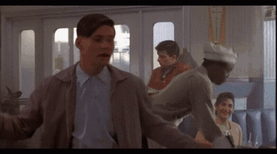 A Man In A Gray Jacket Stands In Front Of A Sign That Says " Fly " GIF