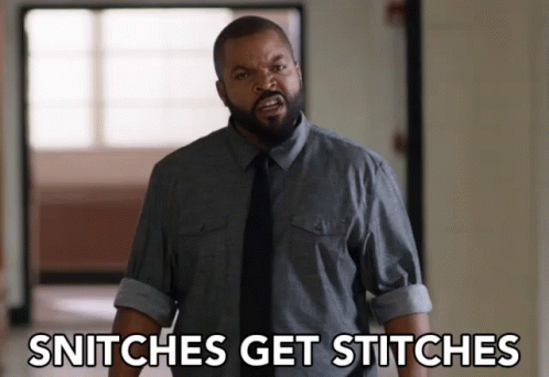 A Man In A Gray Shirt And Black Tie Is Standing In A Hallway And Says Snitches Get Stitches GIF