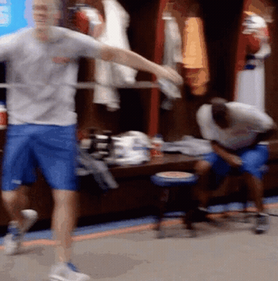 A Man In A Gray Shirt And Blue Shorts Is Dancing In A Locker Room GIF