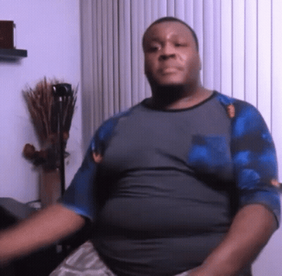 A Man In A Gray Shirt And Blue Sleeves Is Sitting In Front Of A Window . GIF