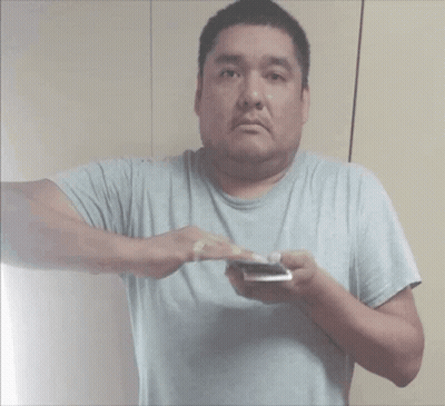 A Man In A Gray Shirt Is Holding A Cell Phone GIF