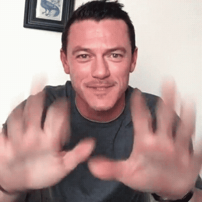 A Man In A Gray Shirt Is Holding His Hands Up In The Air . GIF