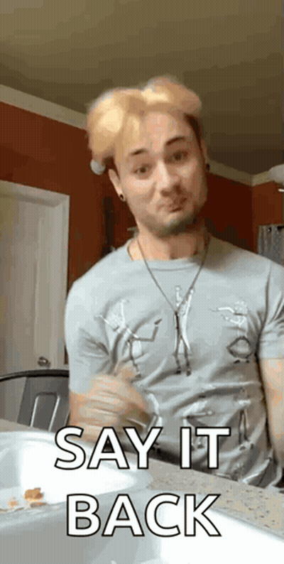 A Man In A Gray Shirt Is Sitting At A Counter And Saying Say It Back . GIF