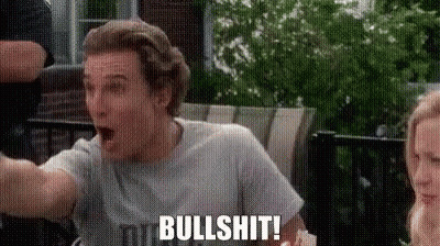 A Man In A Gray Shirt Is Sitting On A Patio With His Mouth Open And A Woman Behind Him . GIF