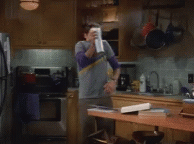 A Man In A Gray Shirt Is Spraying A Can Of Air Freshener In A Kitchen GIF