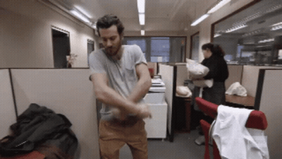 A Man In A Gray Shirt Is Standing In A Cubicle GIF