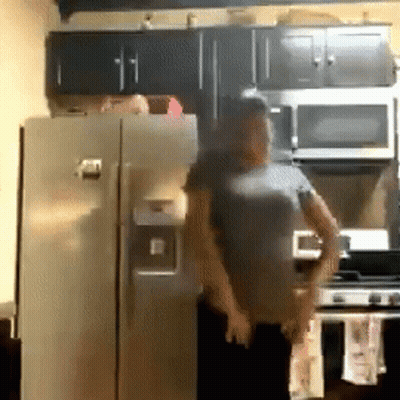 A Man In A Gray Shirt Is Standing In Front Of A Refrigerator In A Kitchen GIF