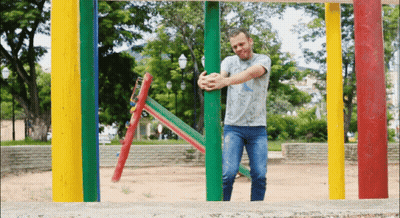 A Man In A Gray Shirt Is Standing In Front Of Colorful Poles GIF