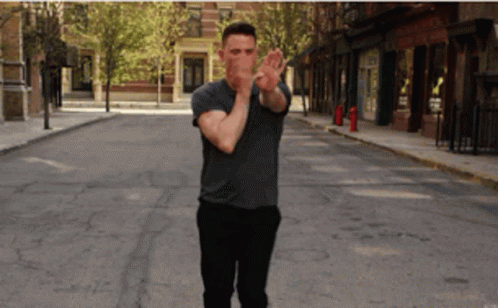 A Man In A Gray Shirt Is Walking Down A City Street GIF