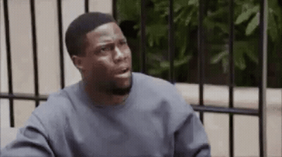 A Man In A Gray Sweater Is Sitting In Front Of A Fence And Making A Funny Face . GIF