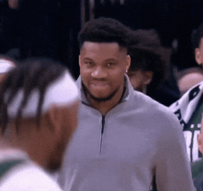 A Man In A Gray Sweater Is Smiling While Talking To Another Man . GIF