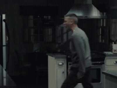 A Man In A Gray Sweater Is Standing In Front Of A Refrigerator GIF