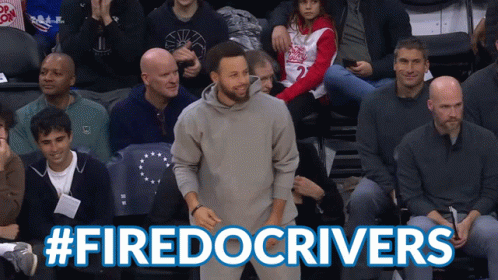 A Man In A Gray Sweatshirt Stands In Front Of A Crowd With The Hashtag #Firedocrivers Above Him GIF
