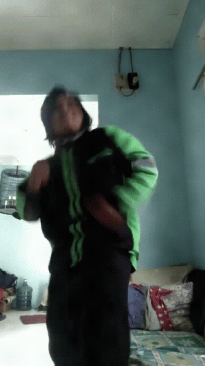 A Man In A Green And Black Jacket Is Dancing In A Living Room GIF