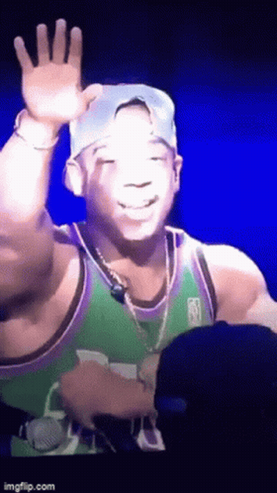 A Man In A Green And Purple Jersey Is Waving At The Camera GIF