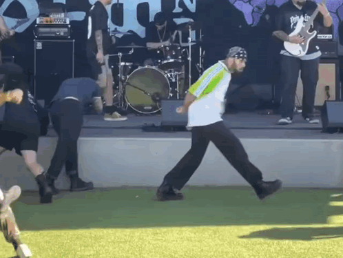A Man In A Green And White Shirt Is Walking On The Grass GIF