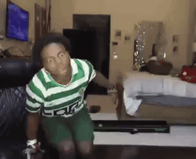 A Man In A Green And White Striped Shirt Is Sitting On A Couch In A Living Room GIF