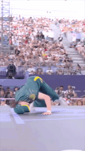A Man In A Green And Yellow Outfit Is Doing A Handstand In Front Of A Crowd . GIF
