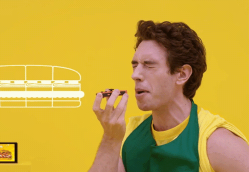 A Man In A Green Apron Eating A Sandwich GIF