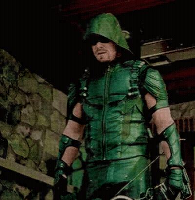 A Man In A Green Arrow Costume Is Holding A Bow And Arrows GIF