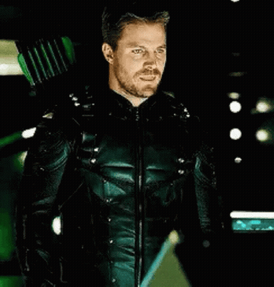 A Man In A Green Arrow Suit Is Holding A Green Arrow Behind His Back . GIF