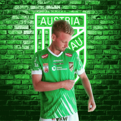 A Man In A Green Austria Jersey Stands In Front Of A Brick Wall GIF