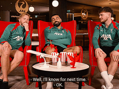 A Man In A Green Aya Shirt Sits With Two Other Men GIF