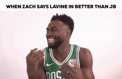 A Man In A Green Basketball Jersey Is Laughing With His Hands Up . GIF