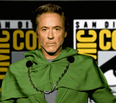 A Man In A Green Cape Stands In Front Of A Comic Con Sign GIF