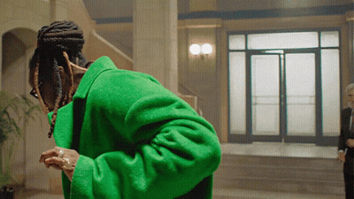 A Man In A Green Coat Stands In Front Of A Doorway GIF
