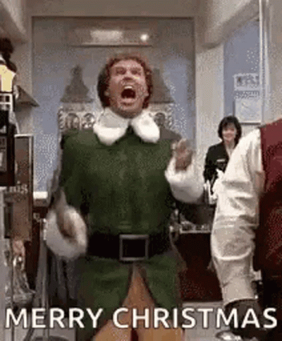 A Man In A Green Elf Costume Is Shouting Merry Christmas While Dancing In A Kitchen . GIF